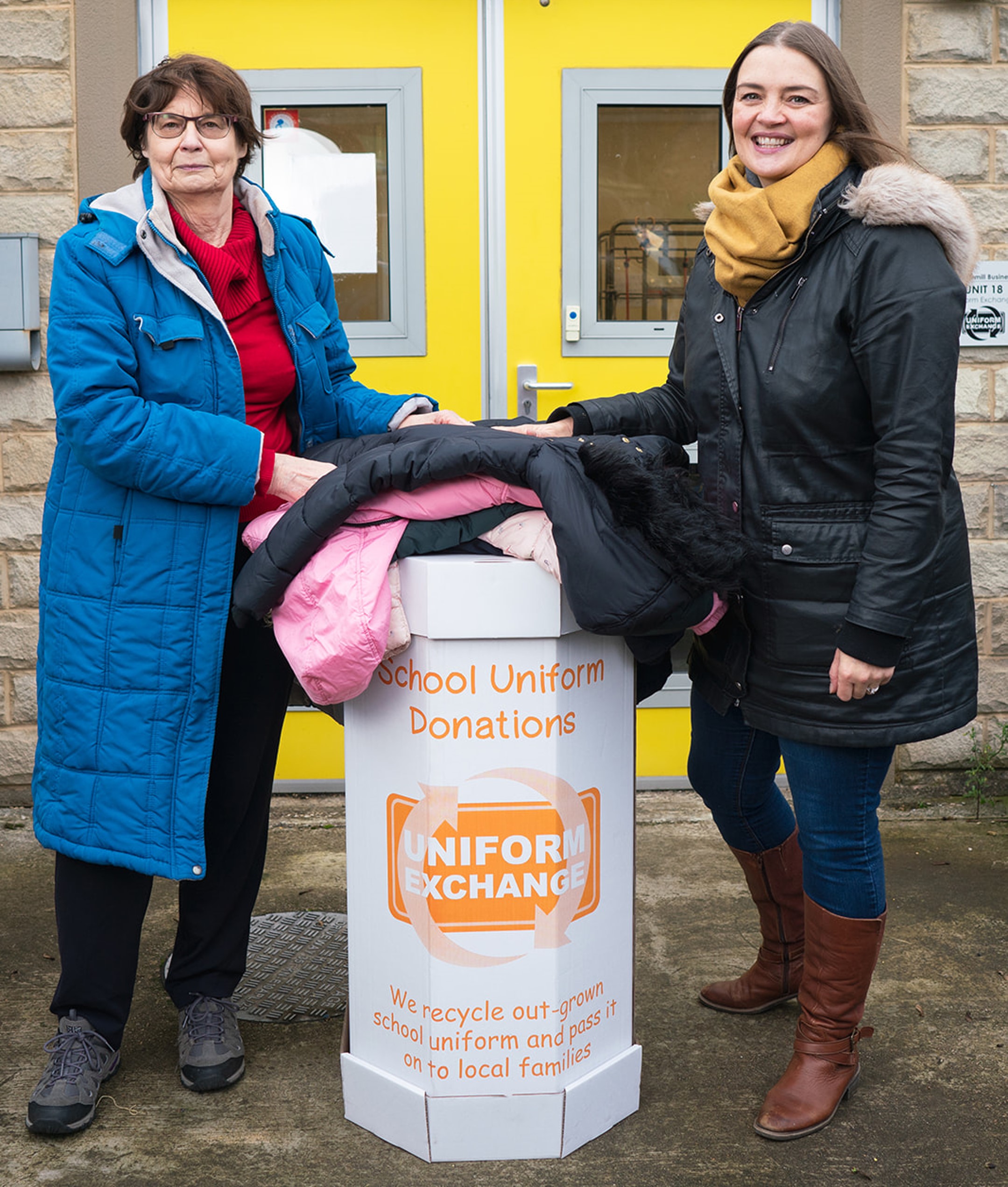 Kate France of Uniform Exchange with a school uniform donation bin and another woman.